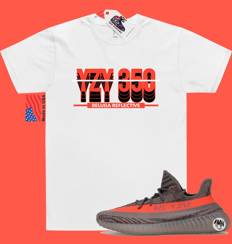 May include: White t-shirt with the text "YZY 350 BELUGA REFLECTIVE" in red and black. A pair of gray and orange Yeezy 350 sneakers are shown below the t-shirt.