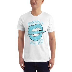 Op de afbeelding: Wit T-shirt met een blauwe cartoonmond met een kleurpotlood waarop "mensen zijn raar" staat. De tekst "NORMAL" staat boven de mond en de tekst "WEIRD" staat onder de mond.