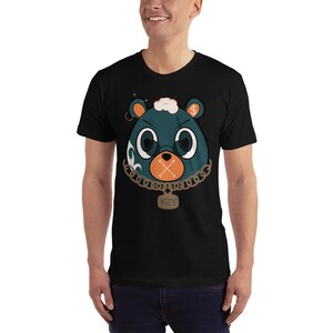 May include: A black t-shirt featuring a cartoon bear wearing a gold chain and a black eye patch. The bear has a dollar sign on its head and an X over its mouth. The text "YZY" is on the chain.