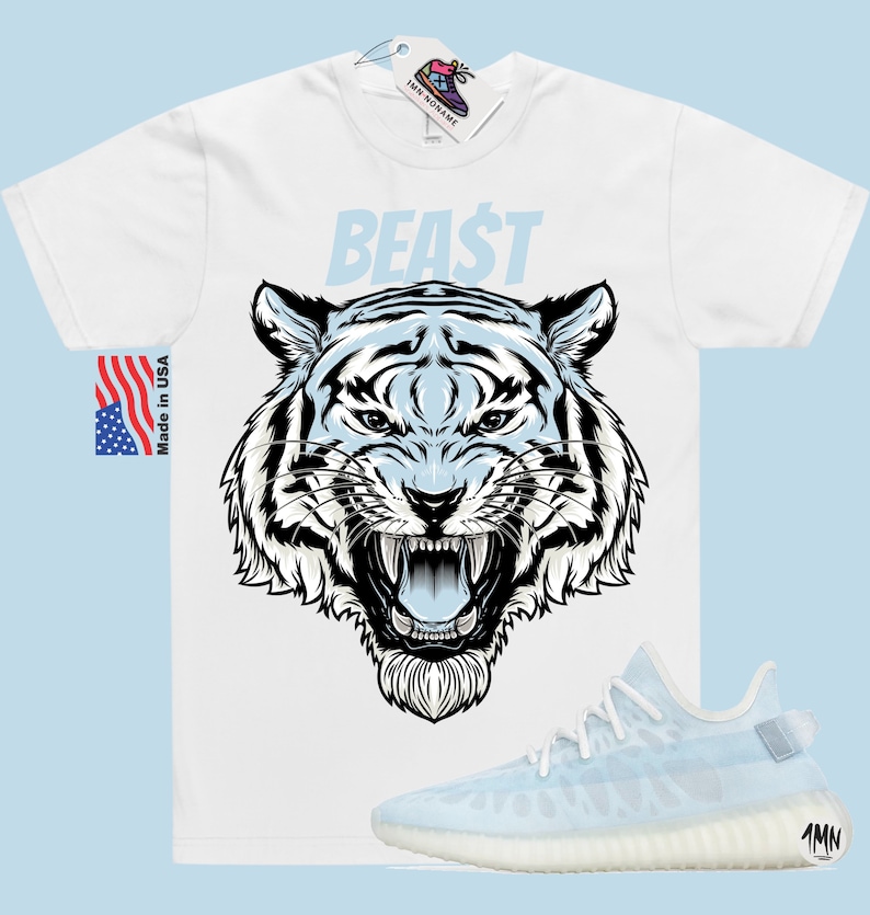 K&ouml;nnte beinhalten: Wei&szlig;es T-Shirt mit einem blauen und wei&szlig;en Tiger-Motiv und dem Wort "BEAST" in Blau. Das T-Shirt wird mit hellblauen und wei&szlig;en Sneakern kombiniert.