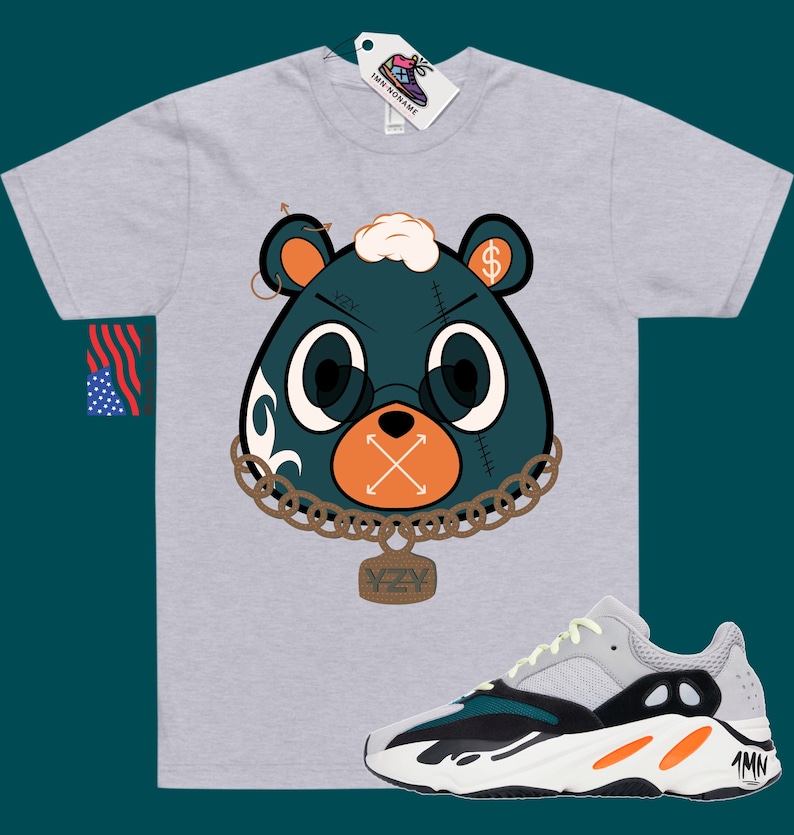 May include: A grey t-shirt featuring a cartoon bear wearing a chain and a tag that reads "YZY". The bear has a dollar sign on its ear and an X over its mouth. The t-shirt is paired with a pair of white, green, and orange trainers with the text "1MN" on the side.