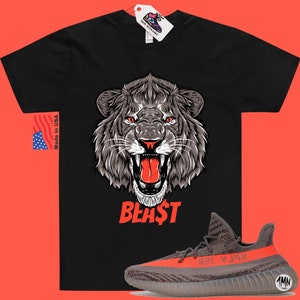 Puede incluir: Camiseta negra con un gr&aacute;fico de un le&oacute;n rugiente y la palabra "BEAST" en rojo. La camiseta se combina con zapatillas grises y naranjas con una raya negra.