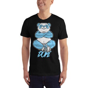 May include: A black t-shirt featuring a blue panda bear sitting with its arms crossed. The panda is wearing a blue outfit and white shoes. The word "DOPE" is written in white below the panda.