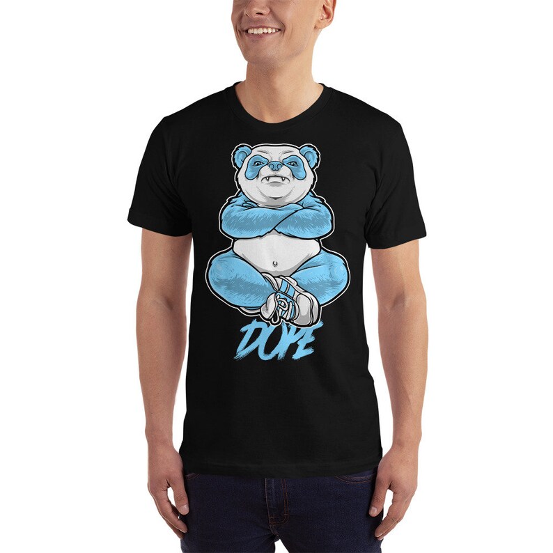 May include: A black t-shirt featuring a blue panda bear sitting with its arms crossed. The panda is wearing a blue outfit and white shoes. The word "DOPE" is written in white below the panda.