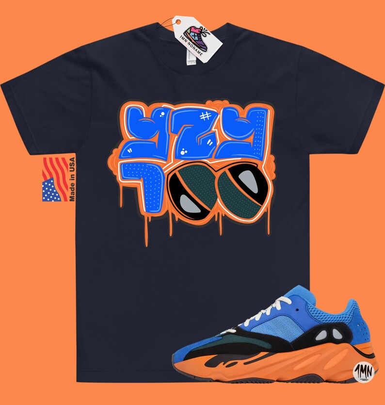 May include: A navy blue t-shirt with a blue and orange graphic that says "YZY 700" with a hashtag symbol. The t-shirt is paired with blue, orange, and black sneakers.