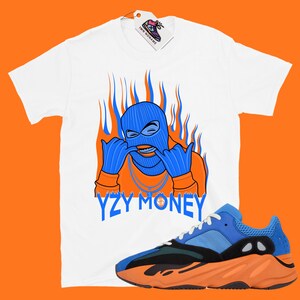 May include: White t-shirt with a blue and orange cartoon character wearing a ski mask and the text "YZY MONEY".  A pair of blue and orange sneakers are also pictured.