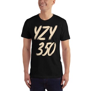 Peut inclure: T-shirt noir avec un motif cr&egrave;me qui dit "YZY 350" dans une police d'&eacute;criture en forme de coups de pinceau.
