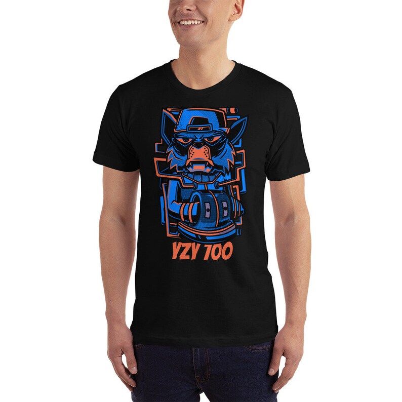 Puede incluir: Una camiseta negra con un gr&aacute;fico azul y naranja de un animal de dibujos animados con un sombrero y sosteniendo un micr&oacute;fono. El texto "YZY 700" est&aacute; impreso debajo del gr&aacute;fico.