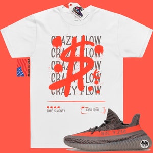 May include: White t-shirt featuring a red spray paint design of a dollar sign and the repeated words "Crazy Flow". The shirt also has the text "Time is Money" and "Cash Flow". A pair of grey and orange trainers are shown below the shirt.