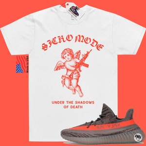 May include: White t-shirt with a red graphic of a cherub holding a gun and the text "Sicko Mode" and "Under the Shadows of Death". A pair of grey and orange sneakers are in the bottom right corner of the image.