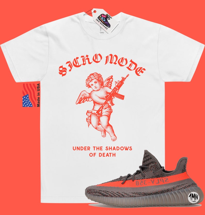 May include: White t-shirt with a red graphic of a cherub holding a gun and the text "Sicko Mode" and "Under the Shadows of Death". A pair of grey and orange sneakers are in the bottom right corner of the image.