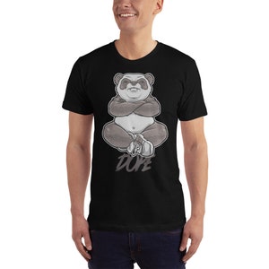 Peut inclure: Un t-shirt noir avec un motif de panda assis, les bras crois&eacute;s. Le panda porte des baskets et le texte "DOPE" est imprim&eacute; en dessous.