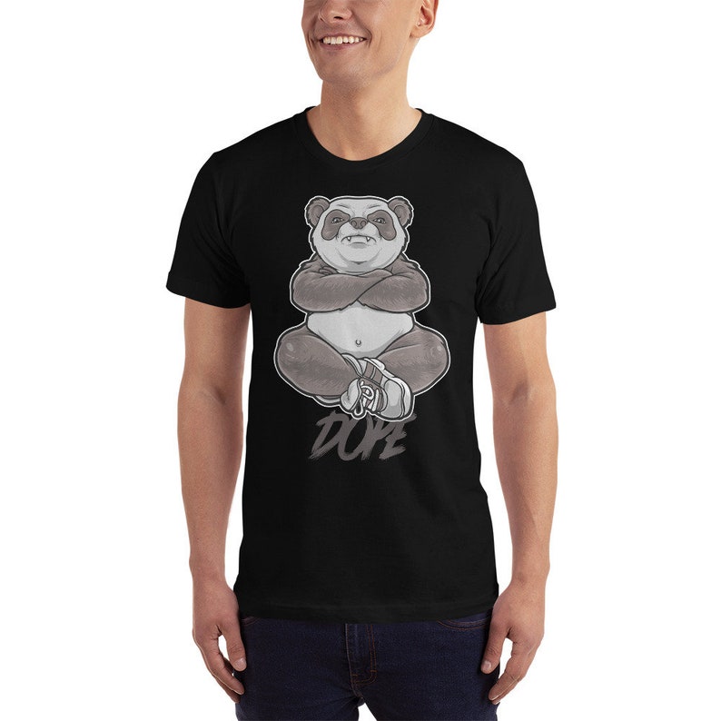 Peut inclure: Un t-shirt noir avec un motif de panda assis, les bras crois&eacute;s. Le panda porte des baskets et le texte "DOPE" est imprim&eacute; en dessous.