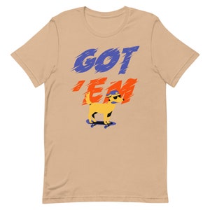 May include: A tan t-shirt with the text "GOT 'EM" in blue and orange letters. A yellow cartoon dog wearing sunglasses and a blue hat is skateboarding.