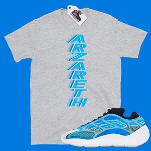 Pu&ograve; includere: Una maglietta grigia con la parola "Zareth" stampata verticalmente in blu e un paio di scarpe da ginnastica blu e bianche.