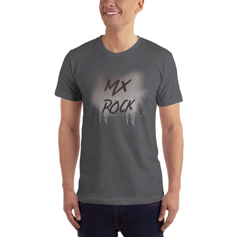 以下が含まれることがあります： 白いスプレーペイント効果と黒い「MX ROCK」の文字が入った濃いグレーのTシャツです。