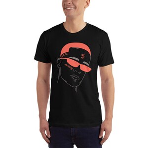 May include: Black t-shirt with a line drawing of a person wearing a coral colored hat and sunglasses. The hat has a dollar sign on it and the sunglasses have the word "money" written on them.