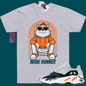 May include: A grey t-shirt with a cartoon cat wearing sunglasses and an orange hoodie. The cat is sitting on a striped background with the text "Wave Runner" below it. A pair of white, green, and orange sneakers are shown below the t-shirt.