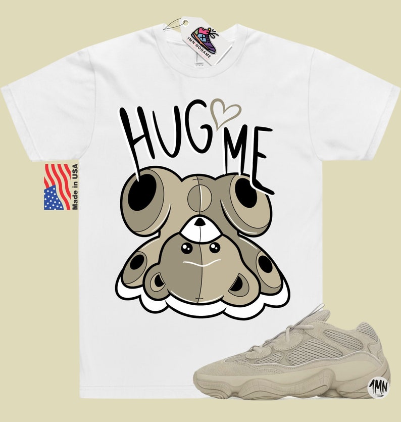 Puede incluir: Camiseta blanca con un oso de peluche de dibujos animados que lleva un coraz&oacute;n y el texto "HUG ME". Un par de zapatillas beige con una parte superior de malla y una suela gruesa.