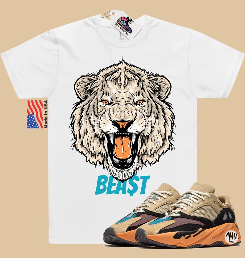 May include: White t-shirt with a detailed lion graphic and the word "BEAST" in blue. Paired with tan, black, and orange sneakers. The shirt has a "Made in USA" tag.
