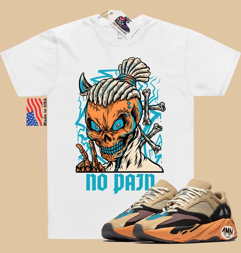 May include: White t-shirt with a graphic of a skull with dreadlocks and the text "no pain". The skull is wearing a blue bandana and has a blue and orange color scheme. A pair of tan, orange, and black sneakers are shown below the t-shirt.