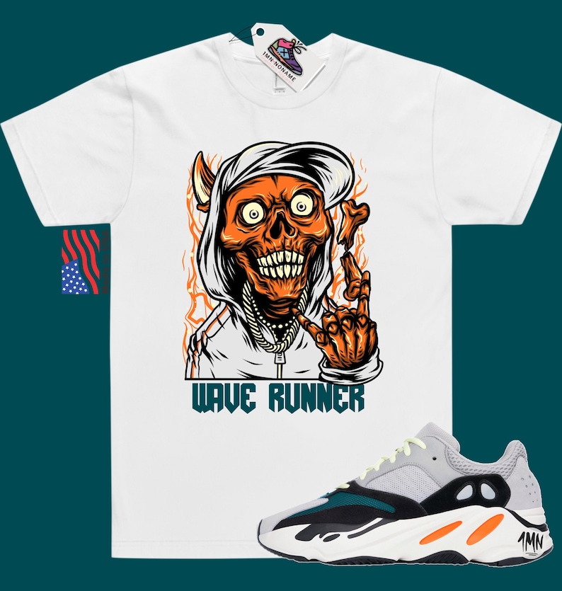 Puede incluir: Camiseta blanca con un gr&aacute;fico de una calavera con una sudadera con capucha y una gorra puesta hacia atr&aacute;s. La calavera es naranja y tiene llamas a su alrededor. El texto "WAVE RUNNER" est&aacute; impreso debajo del gr&aacute;fico. Un par de zapatillas grises, verdes y naranjas se muestran debajo de la camiseta.
