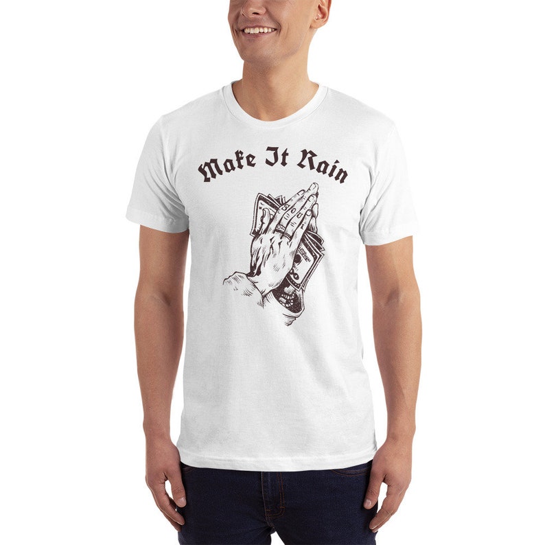 K&ouml;nnte beinhalten: Wei&szlig;es T-Shirt mit einer Grafik einer Hand, die Geld in einer betenden Position h&auml;lt. Der Text "Make It Rain" ist in Schwarz &uuml;ber der Grafik gedruckt.