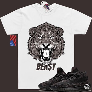 May include: White t-shirt with a black and white illustration of a lion's head and the word "BEAST" printed on the front. A pair of black and grey camouflage sneakers are shown below the shirt.