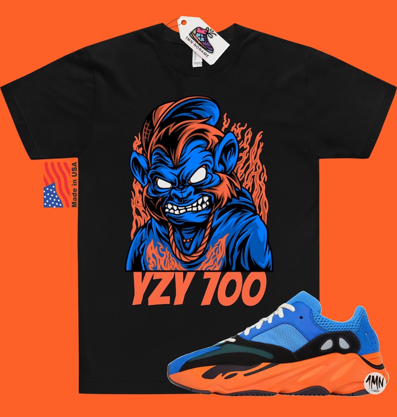 May include: Black t-shirt with a blue and orange cartoon monkey graphic and the text "YZY 700". A pair of blue and orange sneakers with a black sole are in the bottom right corner of the image.