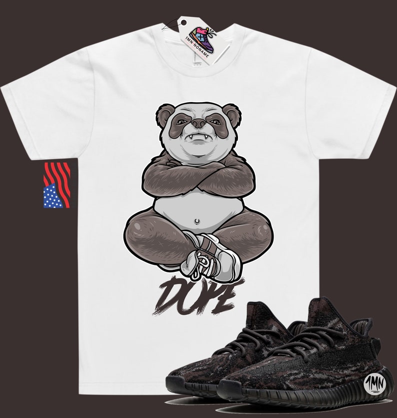 Peut inclure: T-shirt blanc avec un panda dessin anim&eacute; portant une chaussure blanche et assis en tailleur. Le texte "DOPE" est &eacute;crit sous le panda. Une paire de baskets noires et brunes &agrave; motif camouflage est repr&eacute;sent&eacute;e sous le t-shirt.