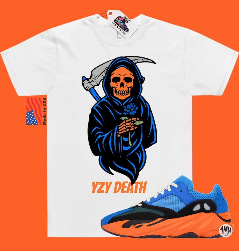 May include: White t-shirt featuring a Grim Reaper graphic holding a blue rose, with the text "YZY DEATH". A pair of blue, black, and orange trainers are in the foreground. The shirt has a tag that says "1MN SONAME".