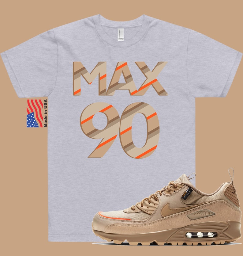 May include: A grey t-shirt with the text "MAX 90" in brown and orange stripes. The shirt is paired with a tan and orange Nike Air Max 90 shoe.