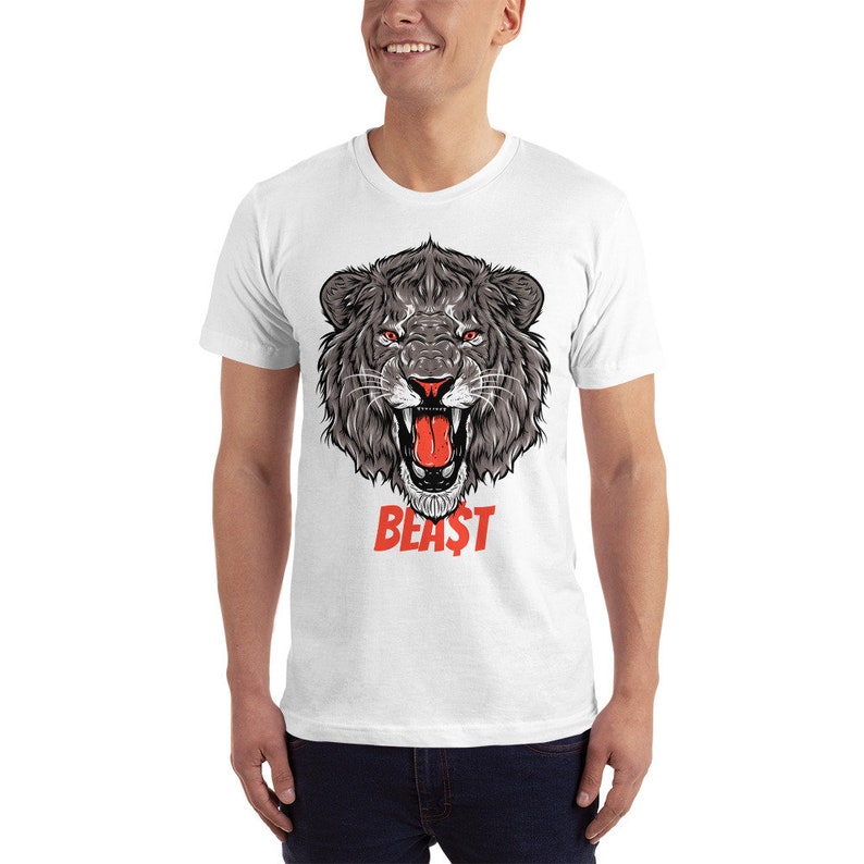 Puede incluir: Camiseta blanca con un gr&aacute;fico de una cabeza de le&oacute;n rugiente en negro y gris con una lengua roja. El texto "BEAST" est&aacute; impreso en rojo debajo de la cabeza del le&oacute;n.