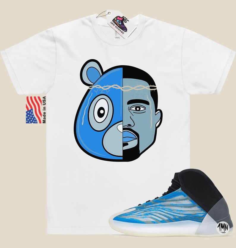 May include: White t-shirt with a blue and grey cartoon image of a bear and a man's face. The image has a crown of thorns on top.  A pair of blue and white sneakers with black accents and a white sole.