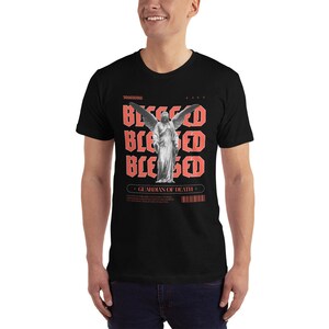 May include: Black t-shirt with a graphic print of an angel with wings and the word "Blessed" repeated four times in red. The text "Guardian of Death" is also printed in red below the angel.