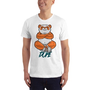 Pu&ograve; includere: Maglietta bianca con una grafica di un panda arancione seduto con le braccia incrociate e la parola "DUDE" scritta in turchese sotto.
