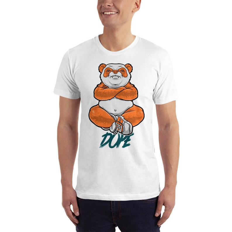 Pu&ograve; includere: Maglietta bianca con una grafica di un panda arancione seduto con le braccia incrociate e la parola "DUDE" scritta in turchese sotto.