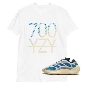 Puede incluir: Camiseta blanca con un estampado gr&aacute;fico "700 YZY" azul y verde. Un par de zapatillas blancas y azules con suela negra.
