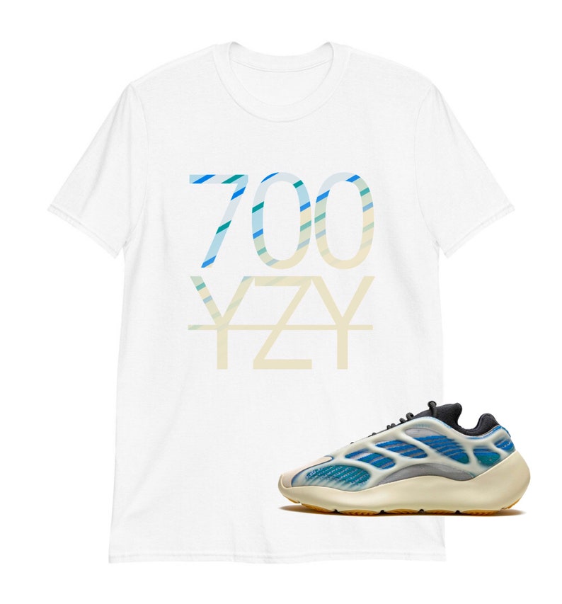 Puede incluir: Camiseta blanca con un estampado gr&aacute;fico "700 YZY" azul y verde. Un par de zapatillas blancas y azules con suela negra.