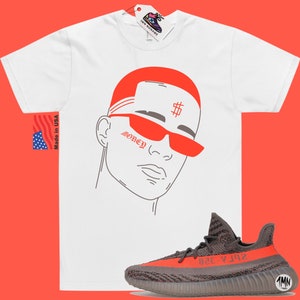 May include: White t-shirt with a red and gray illustration of a person wearing sunglasses and a bandana with the word "Money" and a dollar sign. The t-shirt is paired with gray and red sneakers.