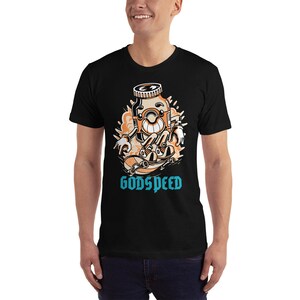 May include: Black t-shirt with a cartoon illustration of a bottle character skateboarding. The bottle is orange and brown with a white face and a blue cap. The text "GODSPEED" is printed in blue below the illustration.