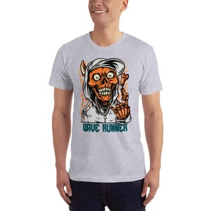 Puede incluir: Una camiseta gris con un gr&aacute;fico de una calavera con capucha haciendo un signo de paz. El texto "WAVE RUNNER" est&aacute; impreso debajo de la calavera.