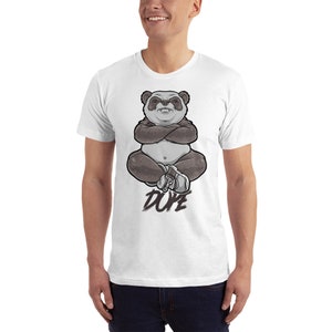 Peut inclure: T-shirt blanc avec un motif de panda assis, les bras crois&eacute;s et portant des baskets. Le texte "DUPE" est imprim&eacute; sous le panda.
