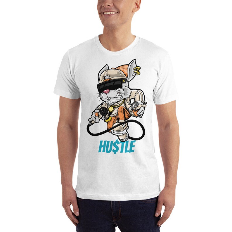 May include: White t-shirt with a cartoon rabbit wearing a hat, sunglasses, and a gold chain. The rabbit is holding a microphone and a spray can. The text "HUSTLE" is printed below the rabbit.