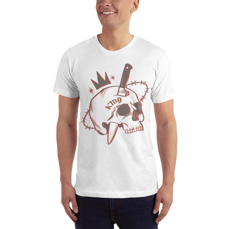 May include: White t-shirt with a red and black graphic of a skull with a knife through it. The skull has a crown on top and the word "king" tattooed on it. The graphic is surrounded by barbed wire.