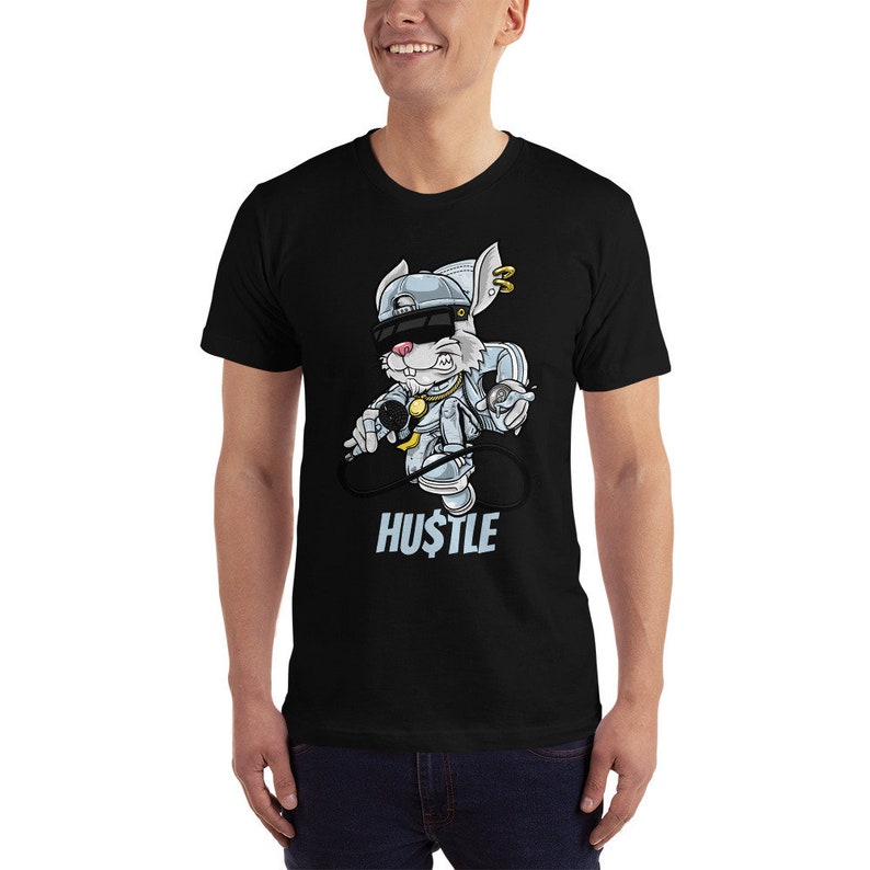 May include: Black t-shirt featuring a cartoon rabbit wearing a backwards baseball cap, sunglasses, and a gold chain. The rabbit is holding a microphone and a spray can. The text "HUSTLE" is printed below the rabbit.
