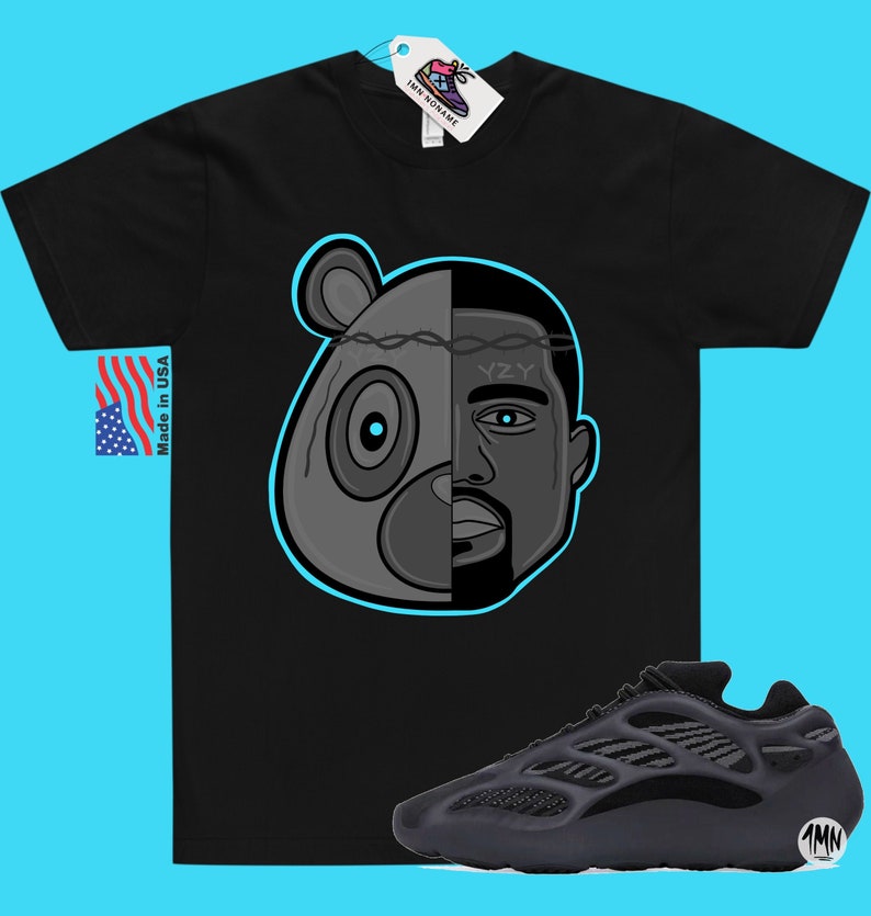 Op de afbeelding: Zwart T-shirt met een afbeelding van een berenkop en het gezicht van Kanye West. De afbeelding is in het midden gesplitst met prikkeldraad dat de twee afbeeldingen scheidt. De tekst "YZY" staat op Kanye West's voorhoofd. Onder het T-shirt is een paar zwarte Yeezy 700 sneakers te zien.