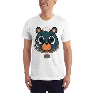 May include: White t-shirt featuring a graphic of a blue bear wearing a gold chain with a tag that says "Yeezy" and a dollar sign on its ear. The bear has a stitched-up face and an orange X over its mouth.
