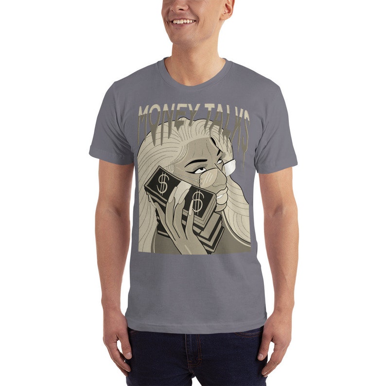May include: A gray t-shirt with a graphic of a woman with blonde hair holding a stack of money to her ear. The text "MONEY TALKS" is written in a stylized font above the woman's head.