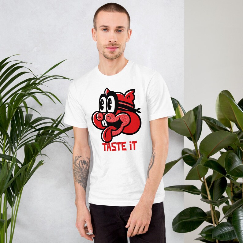 May include: White t-shirt with a red cartoon character wearing a blindfold and the text "TASTE IT" printed on the front.